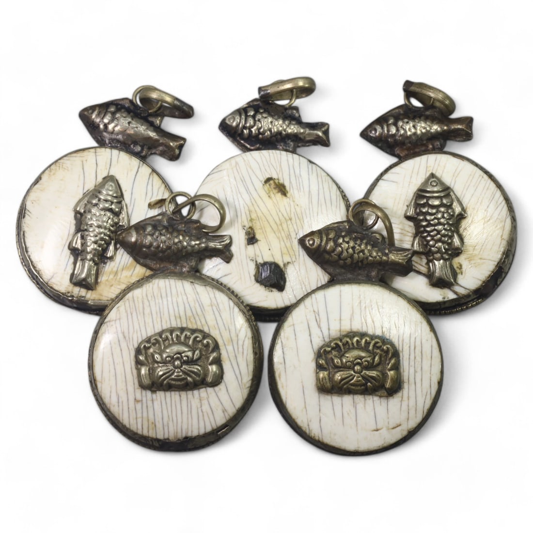 HIMALAYAN: Antique Carved Bone Amulets with Silver Fish Motifs (66g, 4.5cm): This remarkable set of carved bone amulets hails from the Himalayan region, featuring finely detailed silver adornments. Each amulet showcases a central mask motif, symbolizing protection or warding o