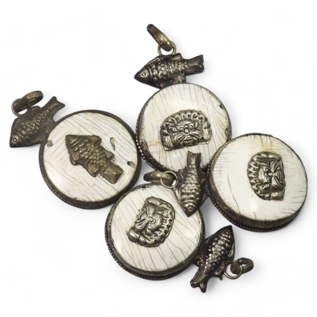 HIMALAYAN: Antique Carved Bone Amulets with Silver Fish Motifs (47g, 4.5cm): This remarkable set of carved bone amulets hails from the Himalayan region, featuring finely detailed silver adornments. Each amulet showcases a central mask motif, symbolizing protection or warding o