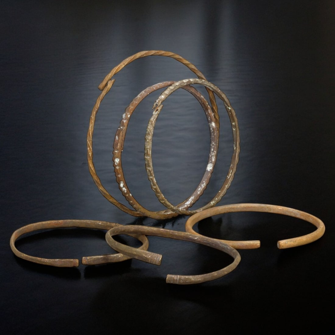 ANTIQUE BRONZE BRACELETS: Lot of Bronze Adornments (80g, 6-8cm): This lot features a collection of antique bronze bracelets, showcasing diverse styles and craftsmanship reflective of different cultural influences. The bracelets vary slightly in size and design, wit