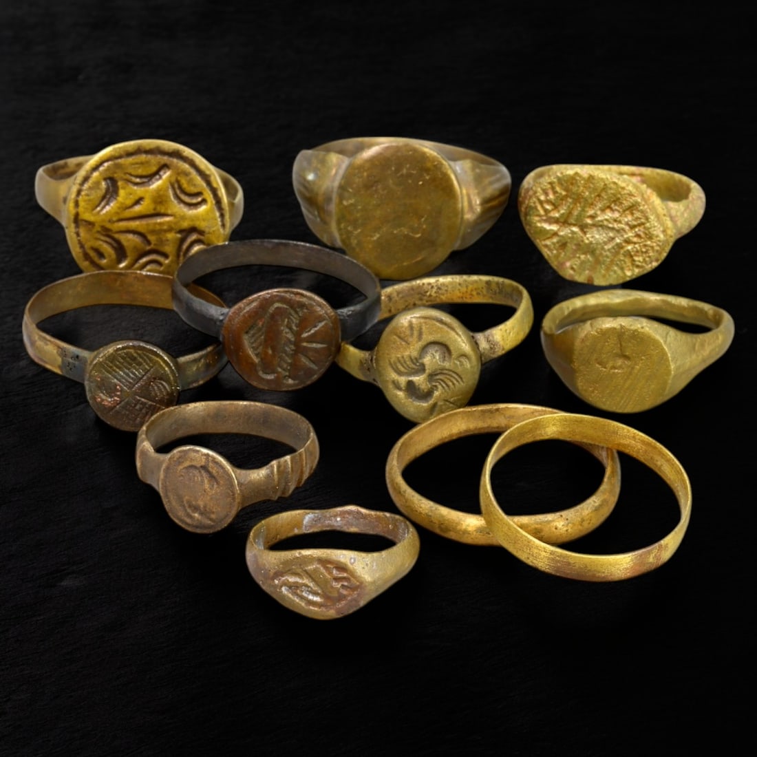 ANCIENT BRONZE RINGS: Gilded Bronze with Engraved Motifs (37g, US Sizes 5-10): This collection of ancient bronze rings showcases a variety of designs, featuring smooth, rounded bezels, engraved geometric motifs, and traces of gilding that hint at their former luster. These rings
