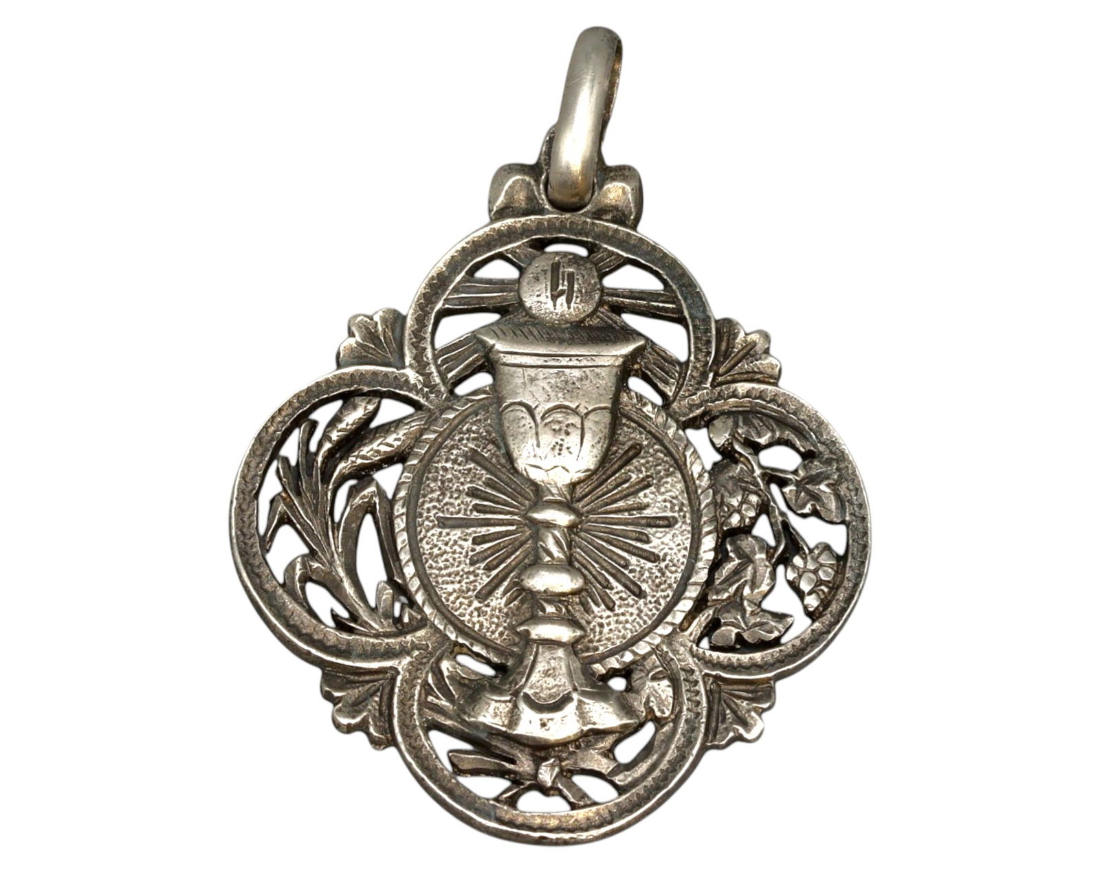 SPAIN: Ornate Silver Eucharistic Medal - Chalice and Grapevine Motif, 19th Century: An exquisite Spanish silver devotional medal, masterfully crafted with a pierced filigree design, featuring a radiant Eucharistic chalice symbolizing the Holy Sacrament of Communion. Encircled by an i
