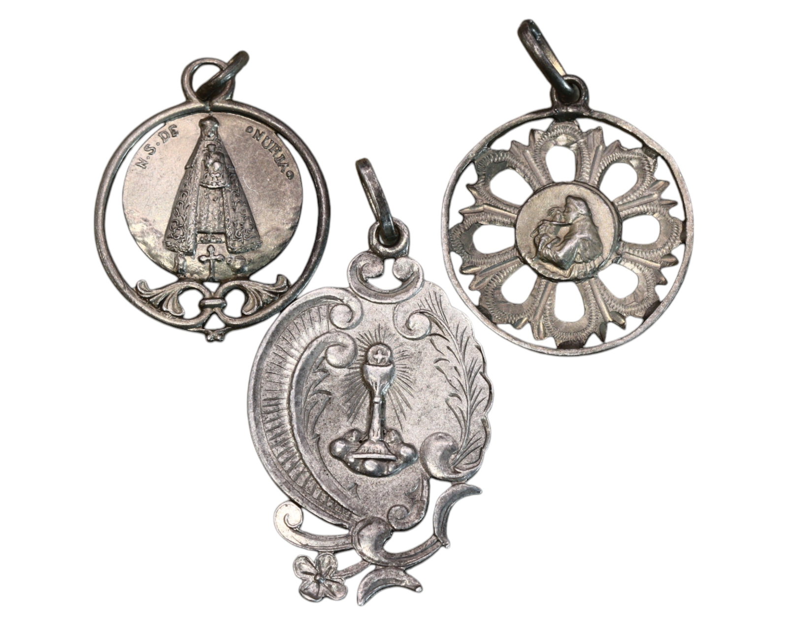 SPAIN: Set of Three Devotional Medals - Silver-Tone, Marian & Eucharistic Symbols, 19th-20th Century: A set of three intricately designed devotional medals, ranging from 2.5 to 3.3 cm and weighing 6.5g, crafted in silver-tone metal. The first medal features Our Lady of Onti?a, encircled by a delicate 