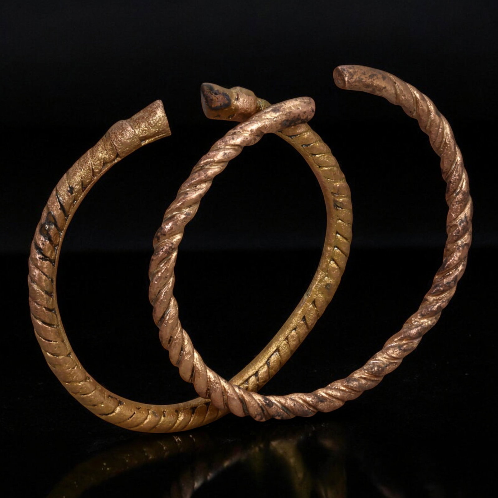 WEST AFRICA: Pair of Twisted Bronze Manilla Currency Bracelets - 7.7-8.2cm, 91g,17th-19th Century: This elegant pair of twisted bronze manilla currency bracelets exemplifies the artistry and economic history of West African trade networks. The distinctive rope-like design, meticulously cast, sugges