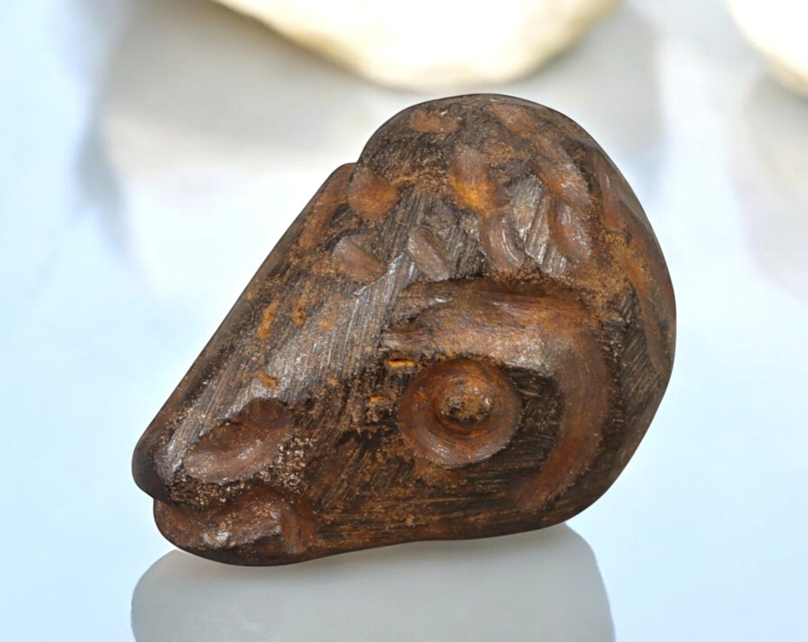 NEAR EAST: Hematite Gazelle Head Amulet - Mesopotamian or Anatolian, 2nd Millennium BCE: A finely carved hematite amulet in the form of a stylized gazelle head, measuring approximately 2.5 x 1.8 cm and weighing 12g. The intricate detailing, including incised patterns and a pronounced spir