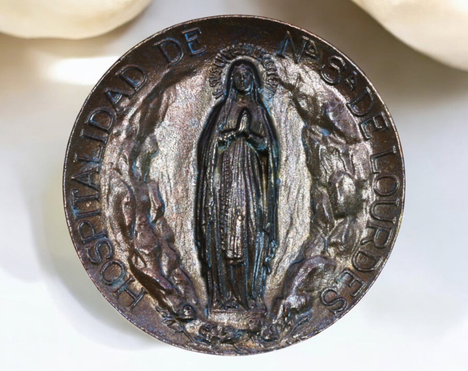 FRANCE: Lourdes Pilgrimage Medal - "Hospitalidad de N.S. de Lourdes", 2.9cm, 10g: A striking vintage bronze-toned pilgrimage medal dedicated to Our Lady of Lourdes, featuring an intricate depiction of the Virgin Mary in the Grotto of Massabielle, surrounded by kneeling pilgrims. Th