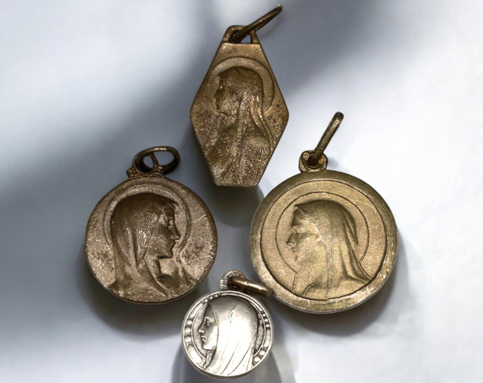 FRANCE: Set of Four Marian Devotional Medals - Lourdes Apparition, 19th-20th Century: A set of four religious medals, measuring 1 to 1.7 cm and weighing 6.3g, featuring Our Lady of Lourdes and the Virgin Mary in profile. Crafted in silver-tone metal, these medals depict St. Bernadette'