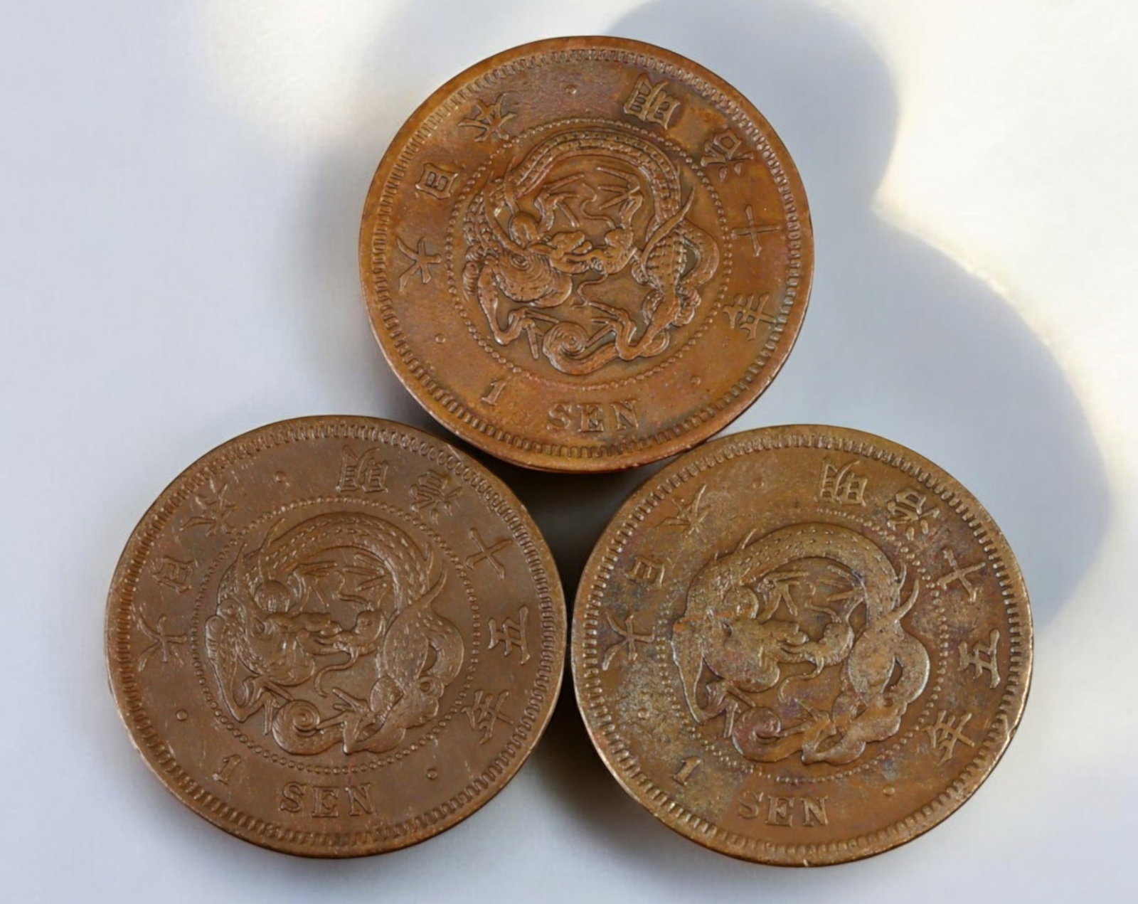 JAPAN: Meiji Era 1 Sen Coin - Copper, Year 10, 15, 15 (1877, 1882, 1882): A set of three Meiji-period 1 Sen coins, struck in copper and weighing 7.13g each with a diameter of 27.9mm, issued under Emperor Mutsuhito (Meiji). The obverse prominently features a coiled dragon, a