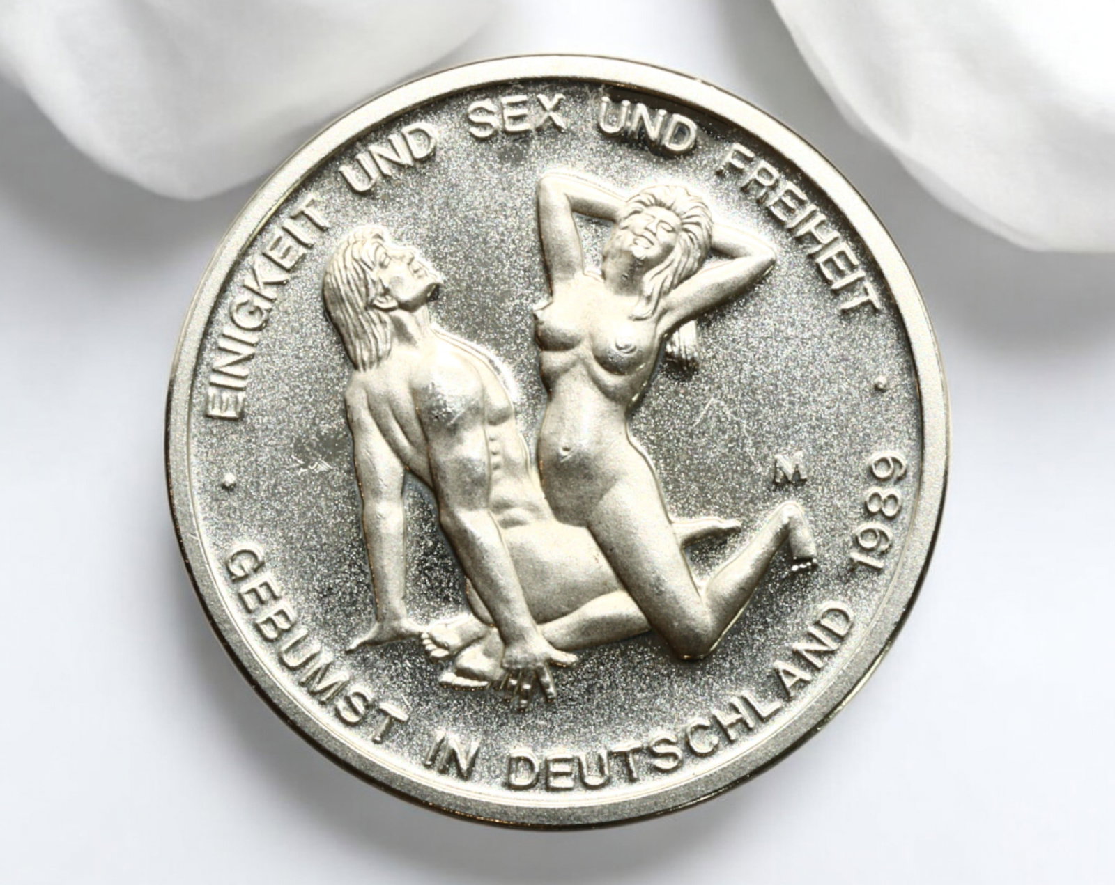 GERMANY: Erotic-Themed Fantasy Token - "Sex Mark," 1989: A risque and satirical fantasy token, struck in a silver-colored alloy, measuring 31mm in diameter and weighing 1.3g. The obverse depicts an erotic scene accompanied by the inscription "EINIGKEIT UND 