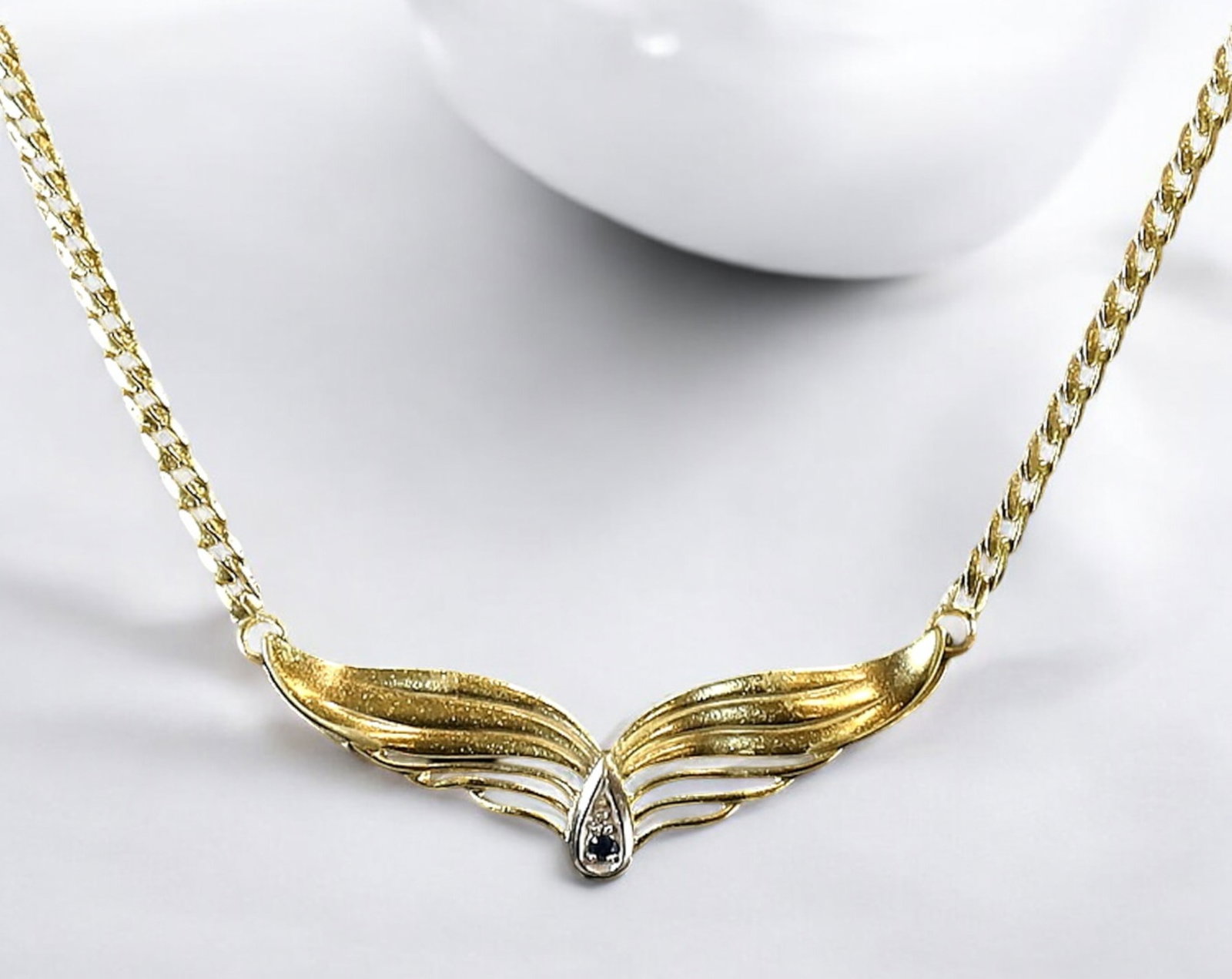 EUROPE: Gold-Tone Angel Wing Necklace with Black Accent Stone, Late 20th Century: A graceful vintage necklace featuring a gold-tone chain measuring 35 cm in length and weighing 7g. The centerpiece is an elegant angel-wing motif, delicately sculpted with flowing curves and accented 