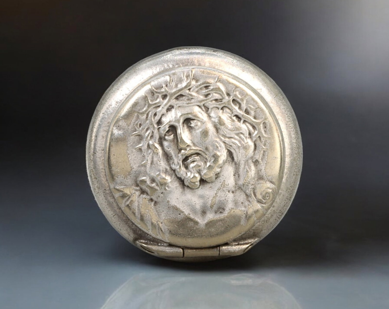 EUROPE: Jesus Christ Reliquary Locket - Silver-Tone Metal, 20th Century: A small yet finely crafted reliquary locket, cast in silver-tone metal, measuring 25mm in diameter and weighing 5g. The front features a detailed high-relief depiction of Christ wearing the Crown of T