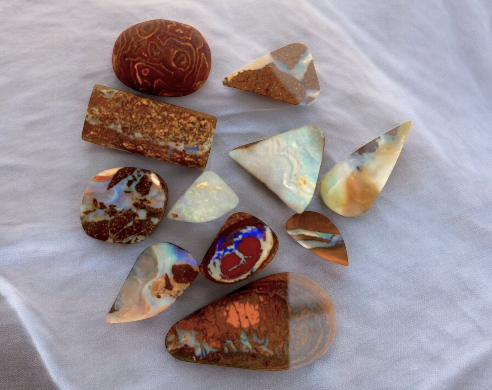 AUSTRALIAN MATRIX BOULDER OPAL - Preform Rough Lot, 11 Pieces, 25.6g, 13-31mm (Images Taken Wet): A dazzling lot of preform Australian matrix boulder opals, with individual sizes. These opals have been rubbed and pre-shaped, highlighting their vibrant natural colors and intricate ironstone matrix 