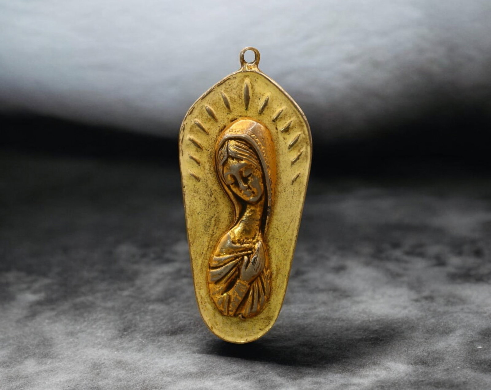 SPAIN: Gilded Devotional Pendant - Madonna with Radiant Halo, 20th Century: A beautifully crafted Spanish religious pendant, featuring a gilded depiction of the Madonna with a radiant halo, symbolizing divine grace and protection. The elongated teardrop shape enhances the del