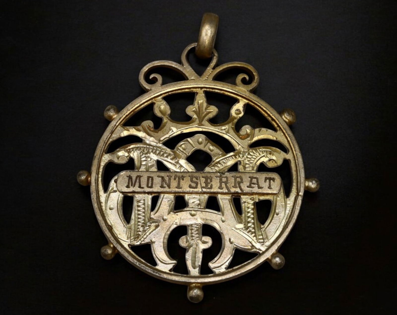 SPAIN: Montserrat Pilgrimage Medal - Ornate Cutout Design, 3g, 3.5x3cm: A beautifully crafted pilgrimage medal from Montserrat, Spain, featuring an elegant cutout design with intricate scrollwork and a crowned "M" monogram, symbolizing the revered Virgin of Montserrat. Th