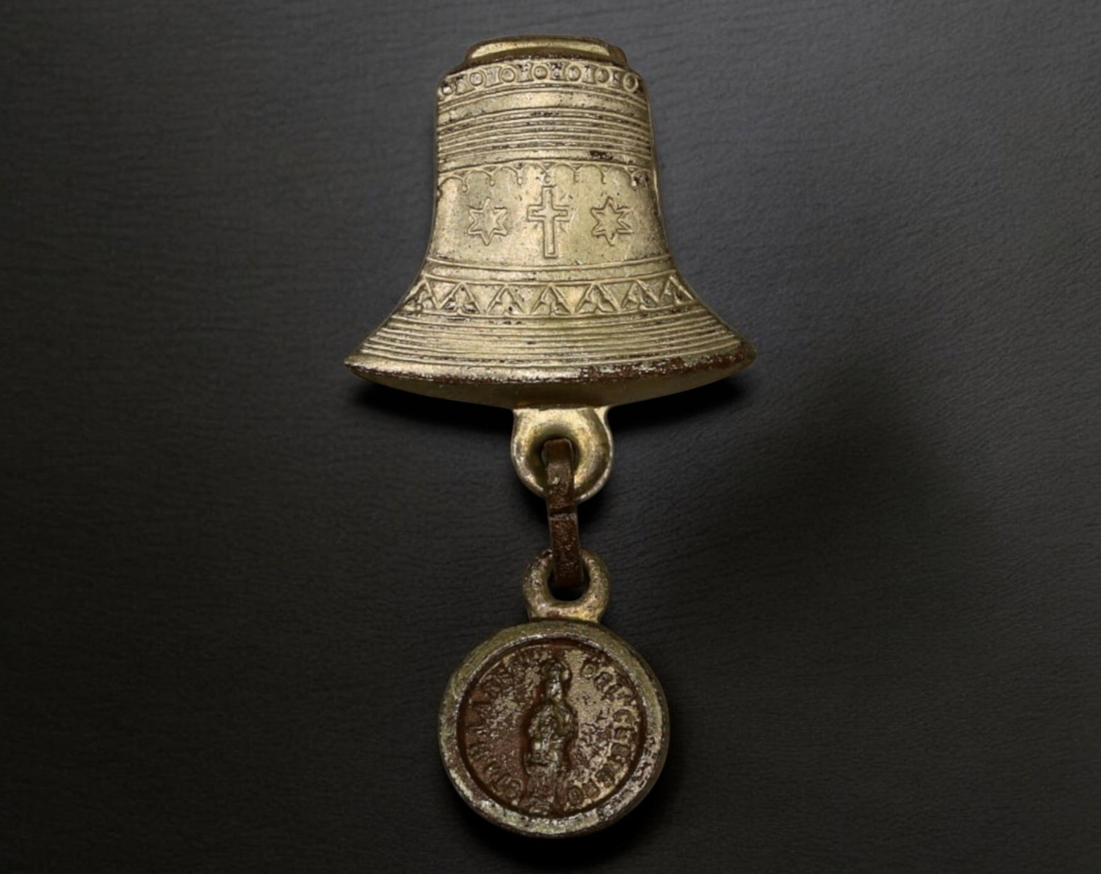 EUROPE: Bell-Shaped Brooch with Hanging Medal - Cross & Star (19th-20th C): An intricately designed bell-shaped religious brooch, featuring delicate engraved patterns, including a central cross flanked by stars, evoking Christian symbolism. Suspended below is a small devotion