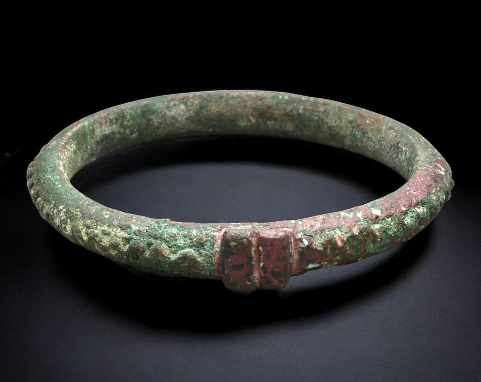 WEST AFRICA: Bronze Currency Bracelet - Cast Form with Central Tab and Braided Motif, 8.5 cm dia.: This distinctive West African bronze bracelet features a rounded band with a central raised tab, flanked by a braided or zigzag motif encircling the exterior. Measuring 8 x 8.5 cm and weighing 114 gra