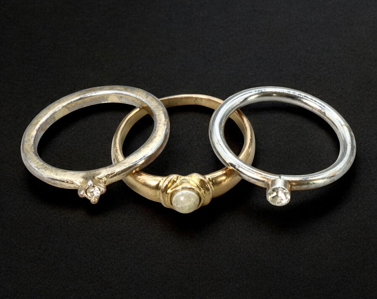 EUROPE: Trio of Minimalist Rings - Silver & Gold-Tone with Simulated Stones, Late 20th Century: A clean and versatile three-ring lot, measuring 2 to 2.3 cm each with a combined weight of 4.8g. Included are two slender silver-tone bands, each set with a small clear round-cut stone in prong and be