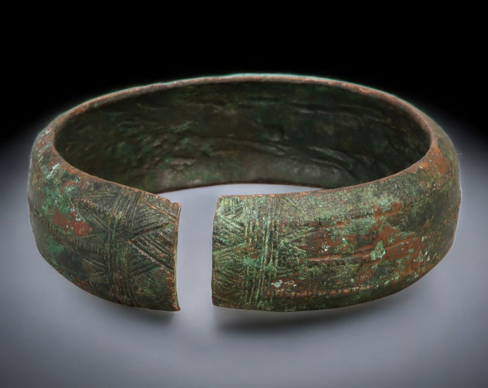 PRE-COLONIAL WEST AFRICA: Flat-Form Bracelet - Cast Bronze, Cross-Hatched Motifs, 6.8 cm dia.: Broad and tactile in form, this cast bronze bracelet from West Africa presents a flattened profile enhanced by incised cross-hatch designs-symmetrical star-like patterns that repeat across the band. M