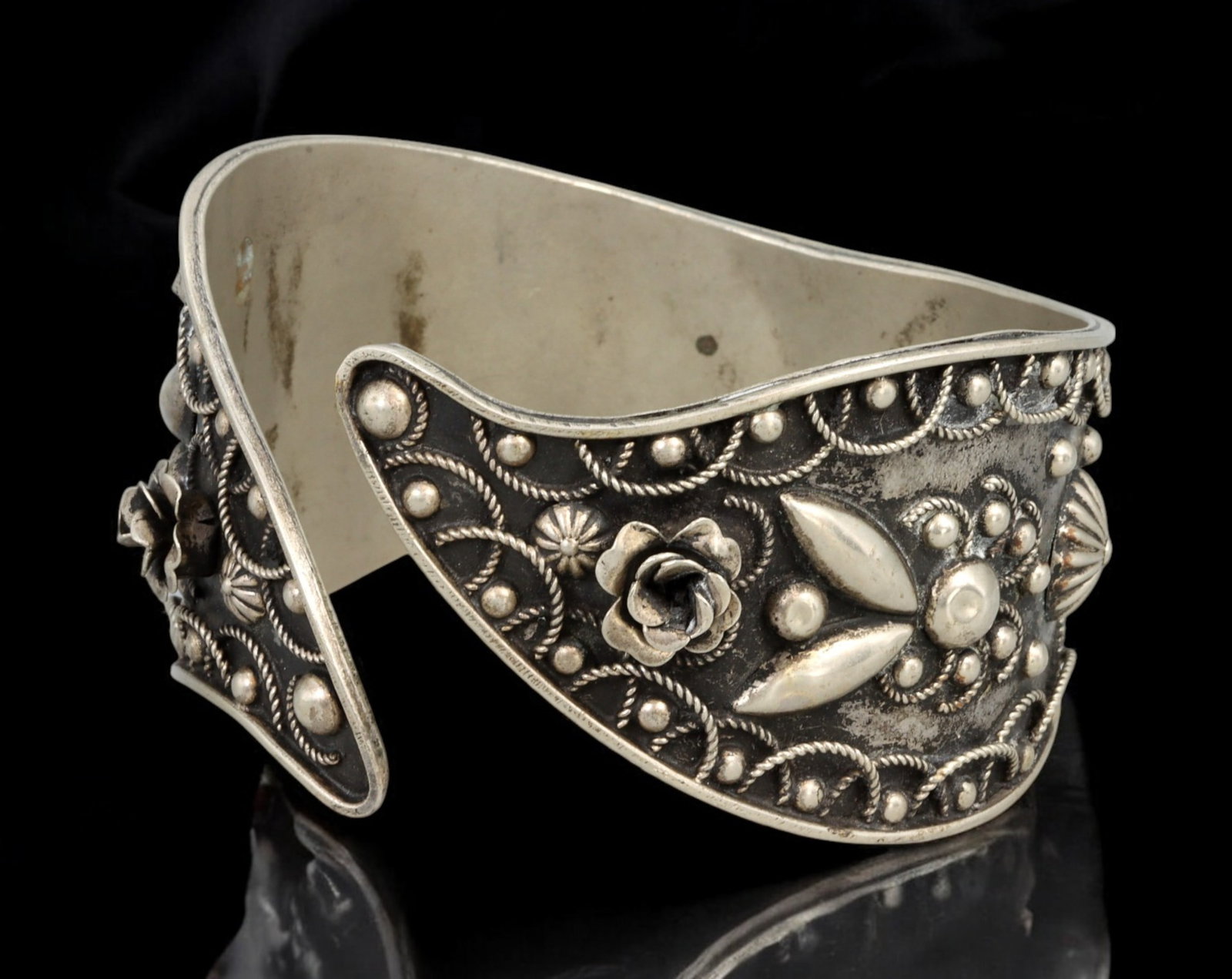 BERBER / NORTH AFRICAN TRIBAL: Bangle - Silver with Granulated Floral Motifs, 7 x 4cm (49g): A richly textured North African tribal-style bangle crafted in silver, featuring raised floral elements and detailed granulation. The asymmetrical silhouette gently curves to embrace the wrist, measur