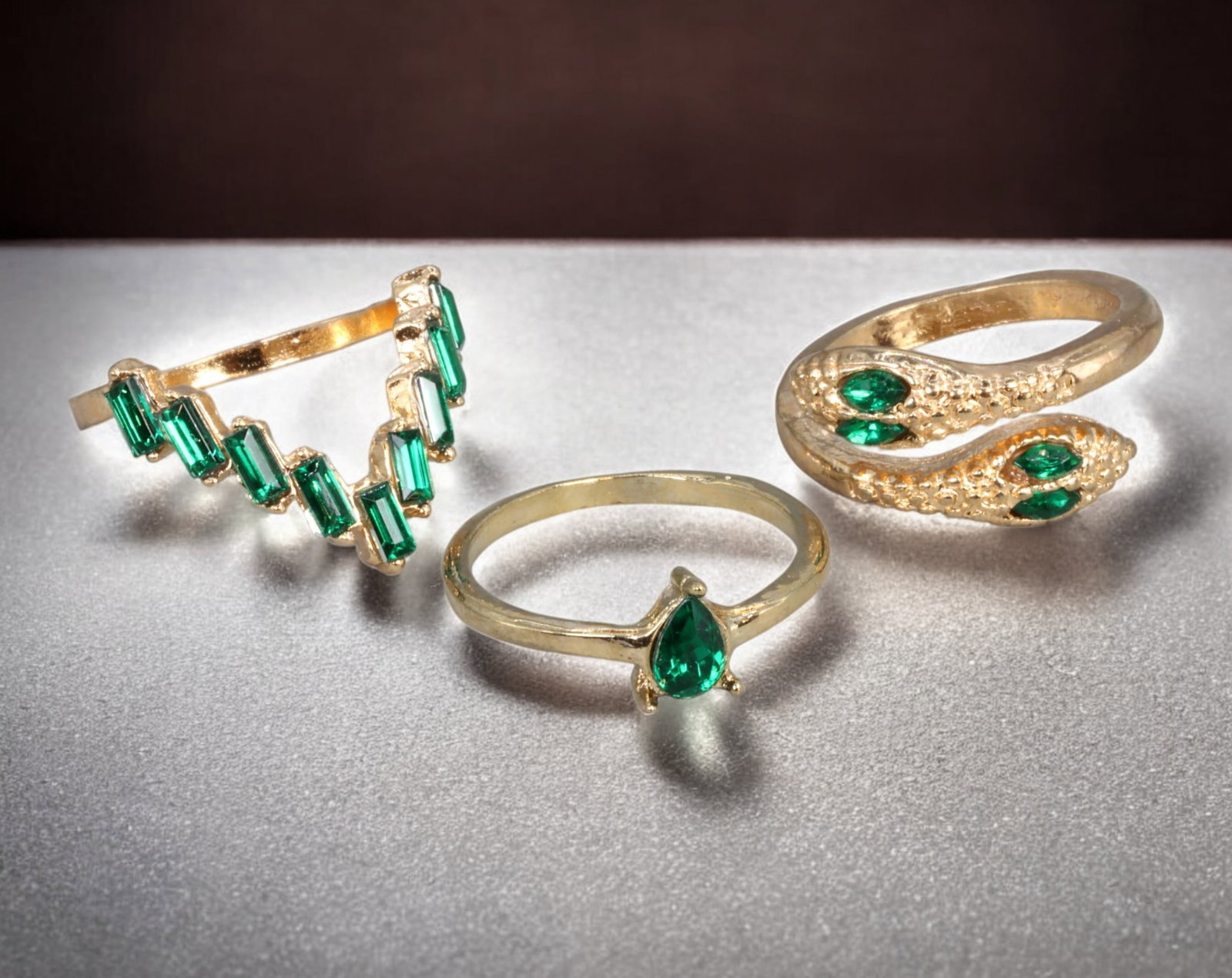 Y2K: Ring Trio -Gold-Tone with Green Faceted Stones,Chevron,Serpent & Teardrop Designs 6.7-7.2cm, 7g: A bold Y2K-inspired ring trio blending playful maximalism with sleek fashion-forward lines. The set includes: a chevron-style ring set with vertically mounted baguette-cut green stones; a teardrop sol
