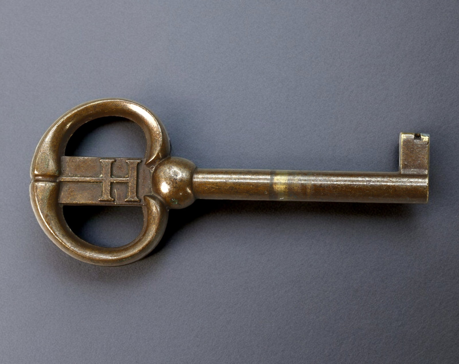 EUROPE: Early 20th Century - Brass Barrel Key, Monogram "H" Bow with Flat-Cut Bit (76x33mm, 22g): Solidly constructed from brass, this early 20th-century European barrel key features a bold oval bow engraved with a central monogram "H," framed by twin reinforcing bars that provide both structure a