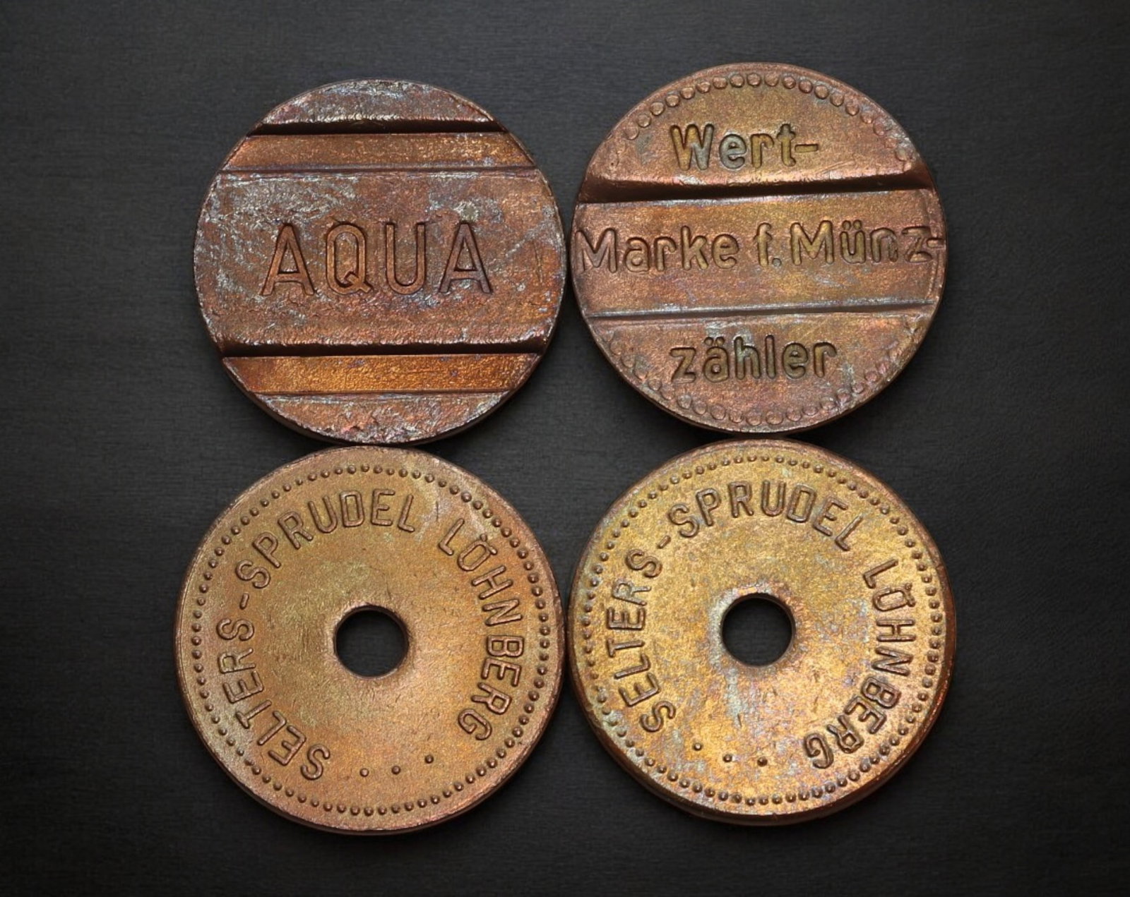 GERMANY: Industrial & Beverage Token Set - Brass, AEG, Selters Sprudel, Aqua, Mid 20th Century: A utilitarian quartet of mid-20th century German brass tokens, measuring 20-21mm and totaling 16.9g. This set includes two holed 'SELTES-SPRUDEL LOHNBERG' tokens from a noted mineral water bottler, in