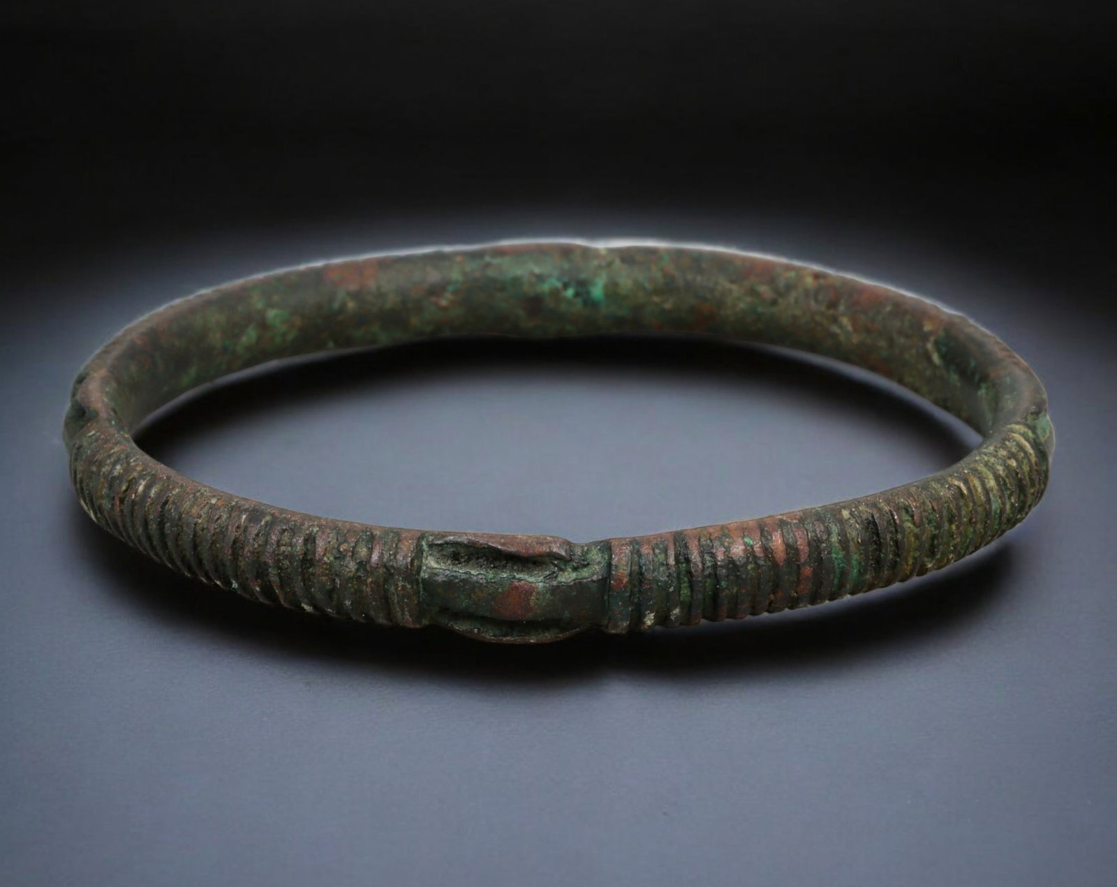 PRE-COLONIAL WEST AFRICA: Trade Bracelet - Cast Bronze, Ribbed Band with Central Join, 7.4 cm dia.: Compact and rhythmically textured, this cast bronze bracelet from West Africa features a continuous ribbed surface flanking a prominent central join. Measuring 7.2 x 7.4 cm and weighing 46 grams, it r