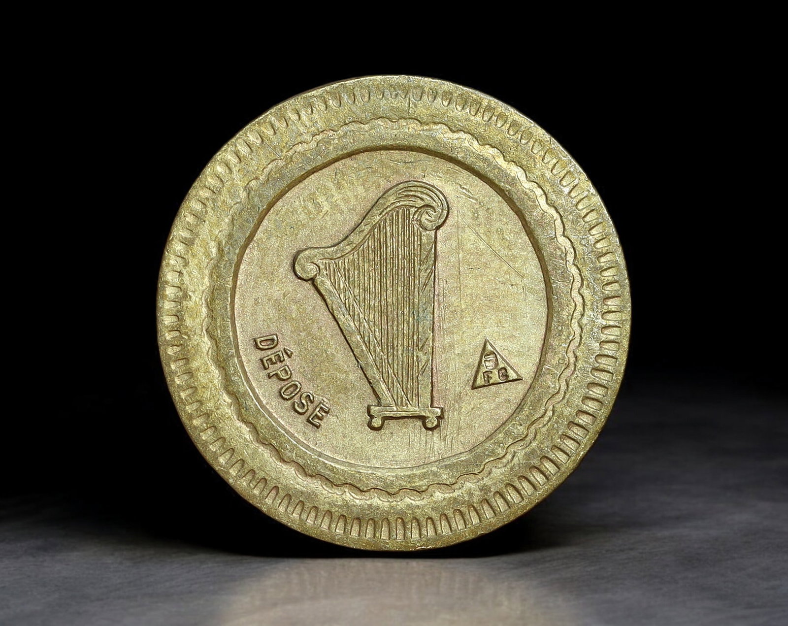 FRANCE: Harp Token - Brass 20 Centimes Coin, ''A Consommer'' with Depose Mark, (18mm, 2.2g): This brass 20 centimes token features a finely detailed vertical harp on one side, accompanied by the inscription ''DEPOSE'' and a small triangular maker's mark, indicating a registered design. The re