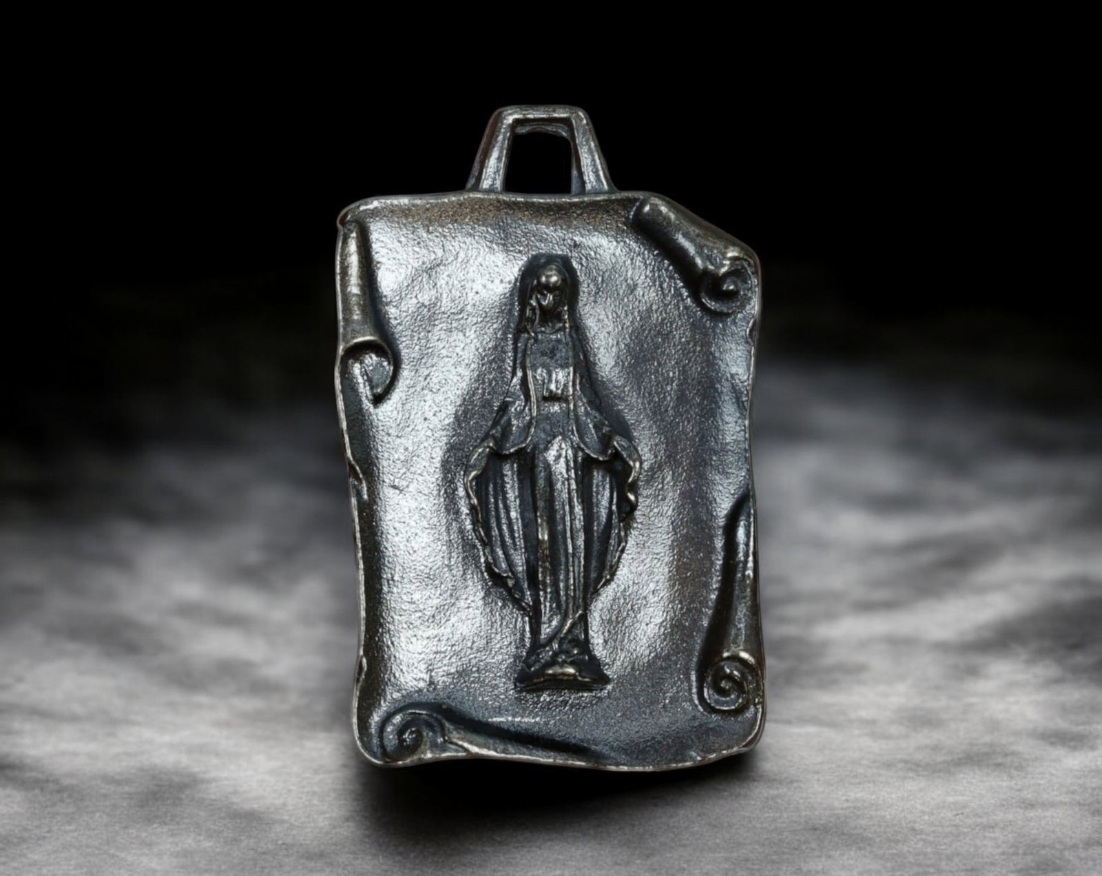 VIRGIN MARY DEVOTIONAL MEDAL - Cast Metal, Scroll-Style Design, 20th Century: An elegantly cast devotional medal featuring the Virgin Mary in a refined, elongated depiction, measuring 2.2 x 3.6 cm and weighing 8.9g. The rectangular design mimics a parchment scroll with curled e