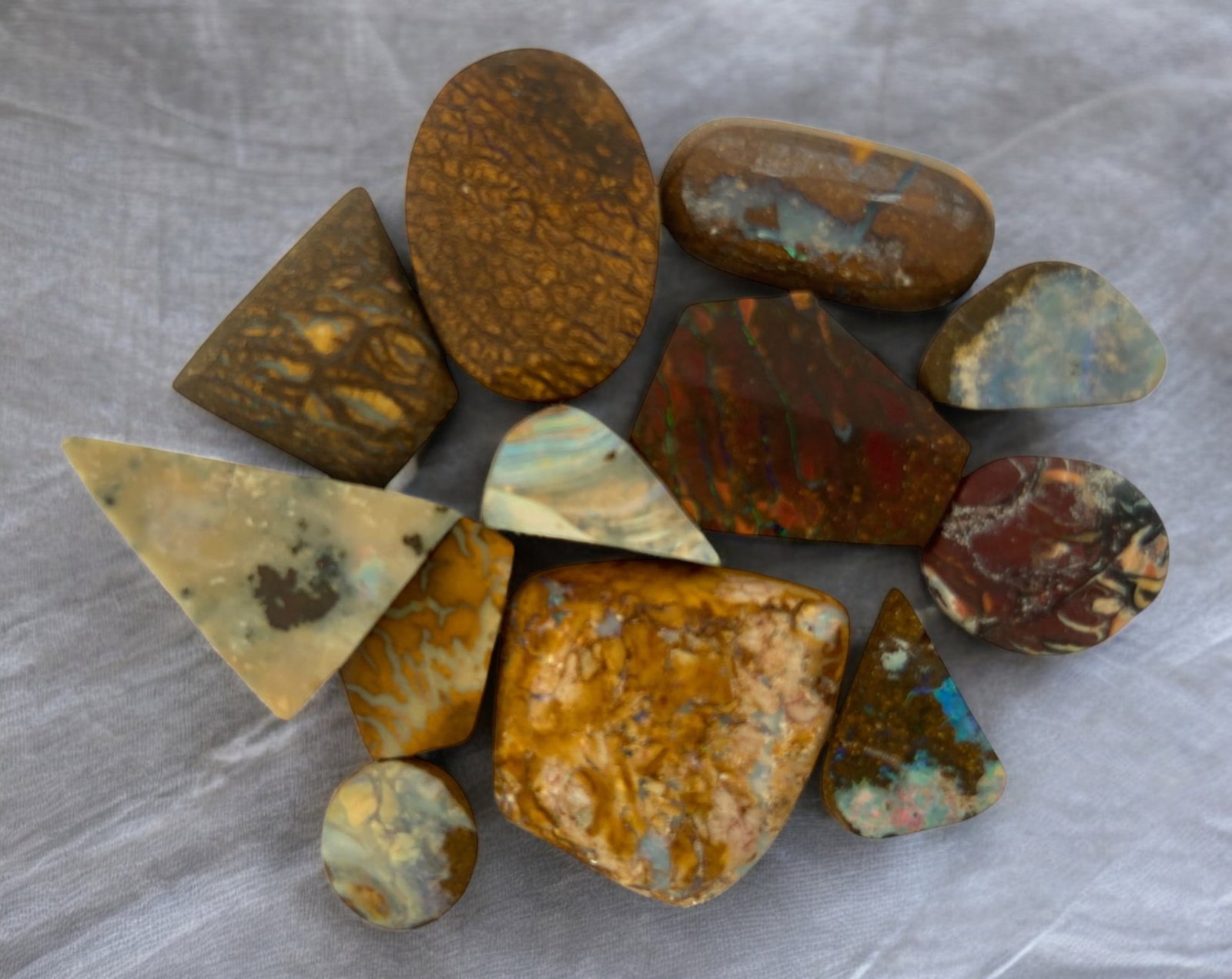 AUSTRALIAN MATRIX BOULDER OPAL - Preform Rough Lot, 12 Pieces, 15.2g, 8.8-21mm (Images Taken Wet): A dazzling lot of preform Australian matrix boulder opals, with individual sizes. These opals have been rubbed and pre-shaped, highlighting their vibrant natural colors and intricate ironstone matrix 