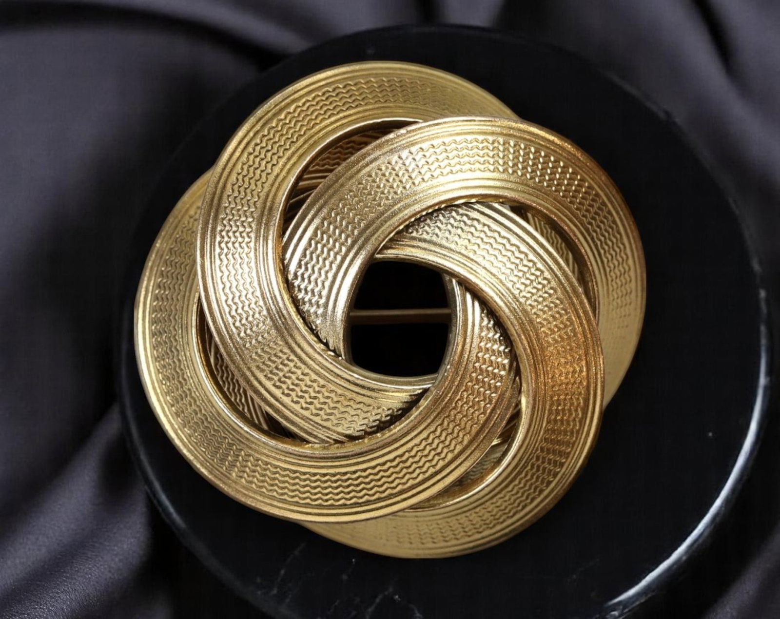 AMERIKANA: VINTAGE MID-CENTURY BROOCH - Interlocked Knot Motif, Textured Finish, 3.5cm: An elegant estate find from the signed line Amerikana, this vintage pin brooch showcases a mid-century interlocked knot motif in rich goldtone. The sculptural loops are finished with alternating high-