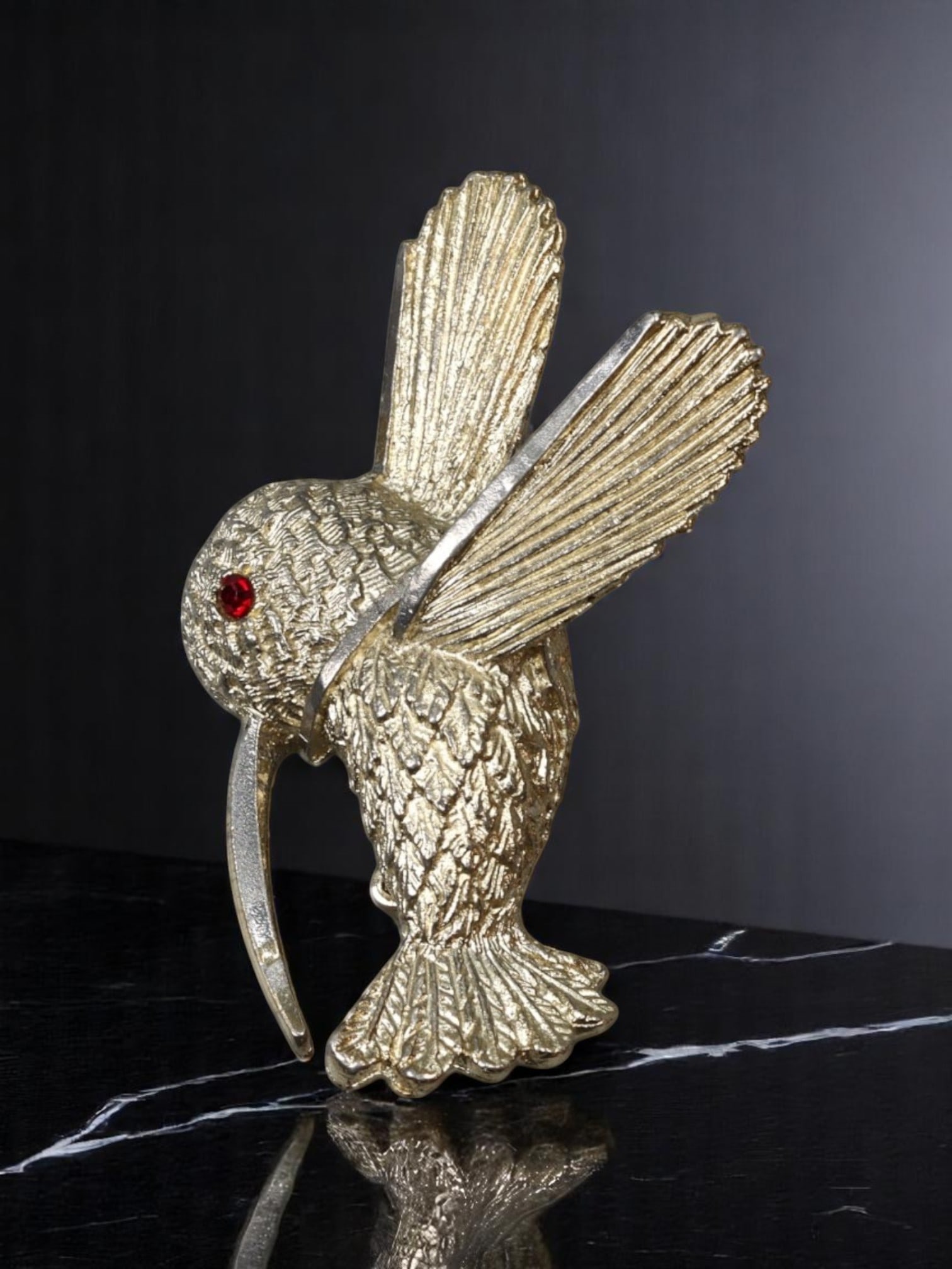 BSK ESTATE FIND: Brooch - Hummingbird Form, Textured Goldtone with Red Stone Eye (4.5x3cm): An estate-sourced brooch by BSK, this goldtone piece captures the grace of a hummingbird mid-hover. Detailed with layered, textured plumage and a ruby-like red eye, the design balances stylized realis