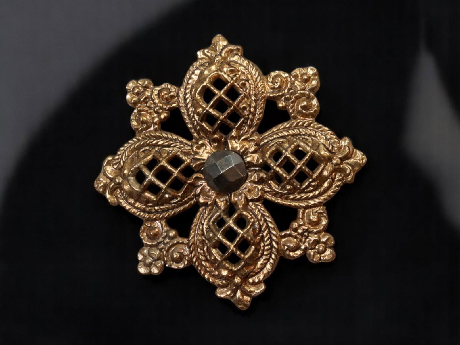 VICTORIAN REVIVAL: Ornate Button or Focal Element - Gilt Latticework with Faceted Center (3cm): An elaborate Victorian Revival piece showcasing intricate openwork lattice patterns framed by richly sculpted scrolls and floral flourishes. A single faceted, dark-toned stone-like element anchors the