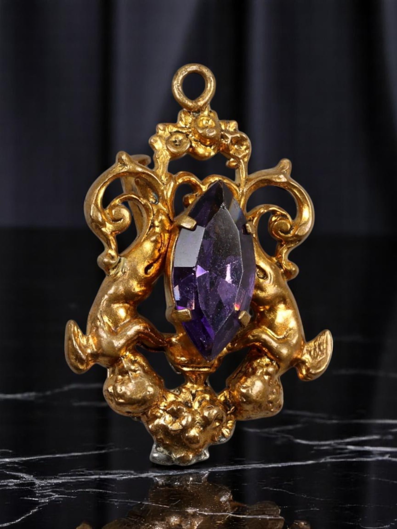VICTORIAN REVIVAL: Pendant - Cherubs with Amethyst-Like Center, Ornate Goldtone Finish (3x2.5cm): An ornate Victorian Revival pendant featuring a deeply sculptural design with twin cherubs and scrollwork surrounding a marquise-cut amethyst-like center stone. Finished in a rich antique goldtone, th