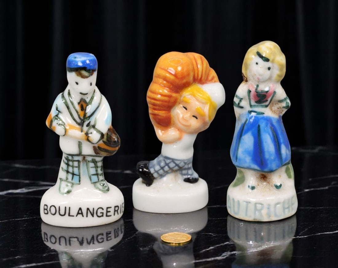 FRENCH: Feve Trio - Bakery & Regional Dress Themes, Hand-Glazed Porcelain (3 pcs, 3-3.5 cm): A cheerful and collectible trio of hand-glazed French feves celebrating iconic elements of culinary and cultural identity. The set includes a baguette-toting figure labeled 'BOULANGERIE,' a smiling ba