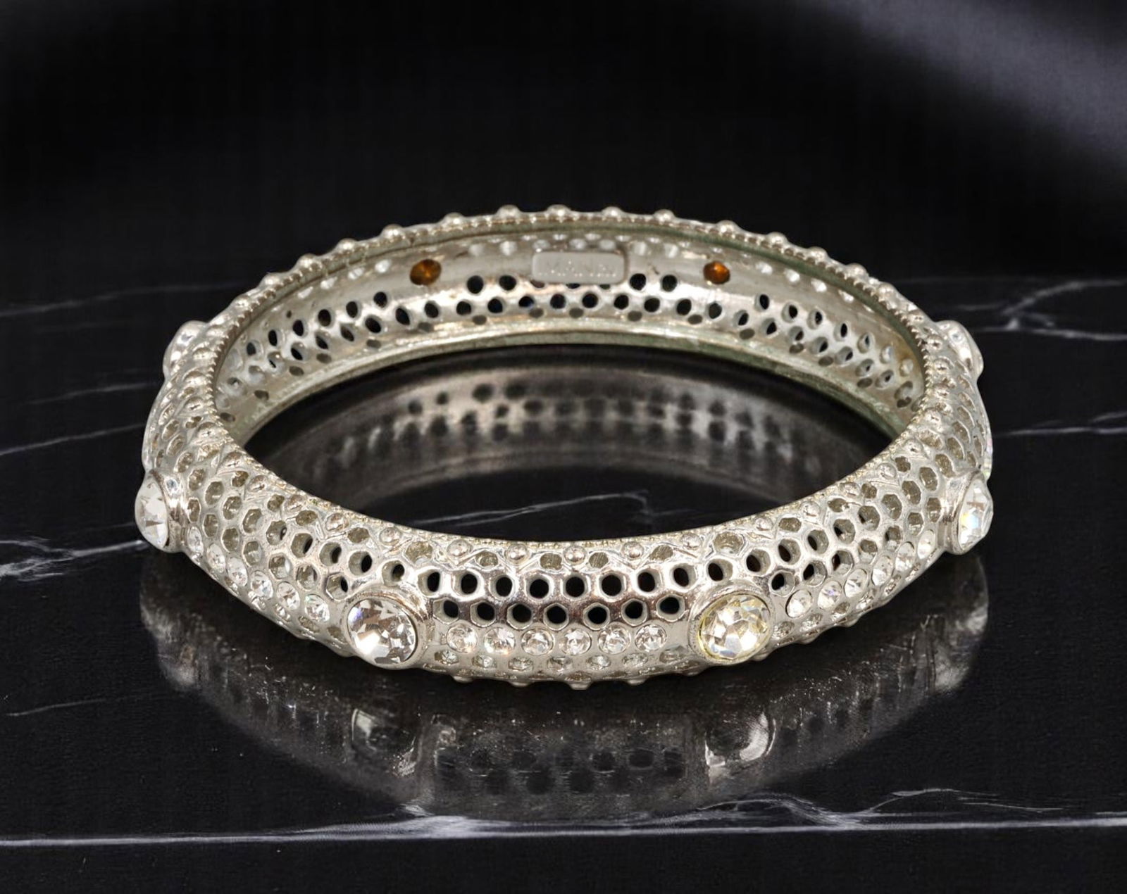 Bangle - IMAN CN, Pierced Silvertone with Brilliant-Cut Accents (9cm): A striking bangle in sculptural silvertone metal, this piece features a bold pierced lattice design and raised beading, accented with clear brilliant-cut stones set rhythmically around the outer surfa