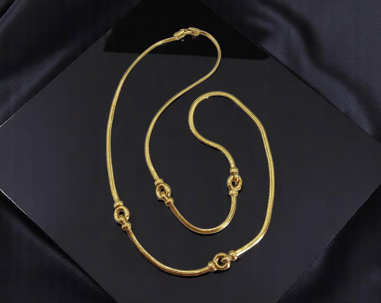 Knot Station Necklace - Polished Snake Chain with Interlinked Rings, Goldtone (72 cm): Subtle and sculptural, this 72 cm necklace offers a refined take on minimalist design with its gleaming goldtone snake chain punctuated by four knotted-ring stations. Each interlinked loop adds soft t