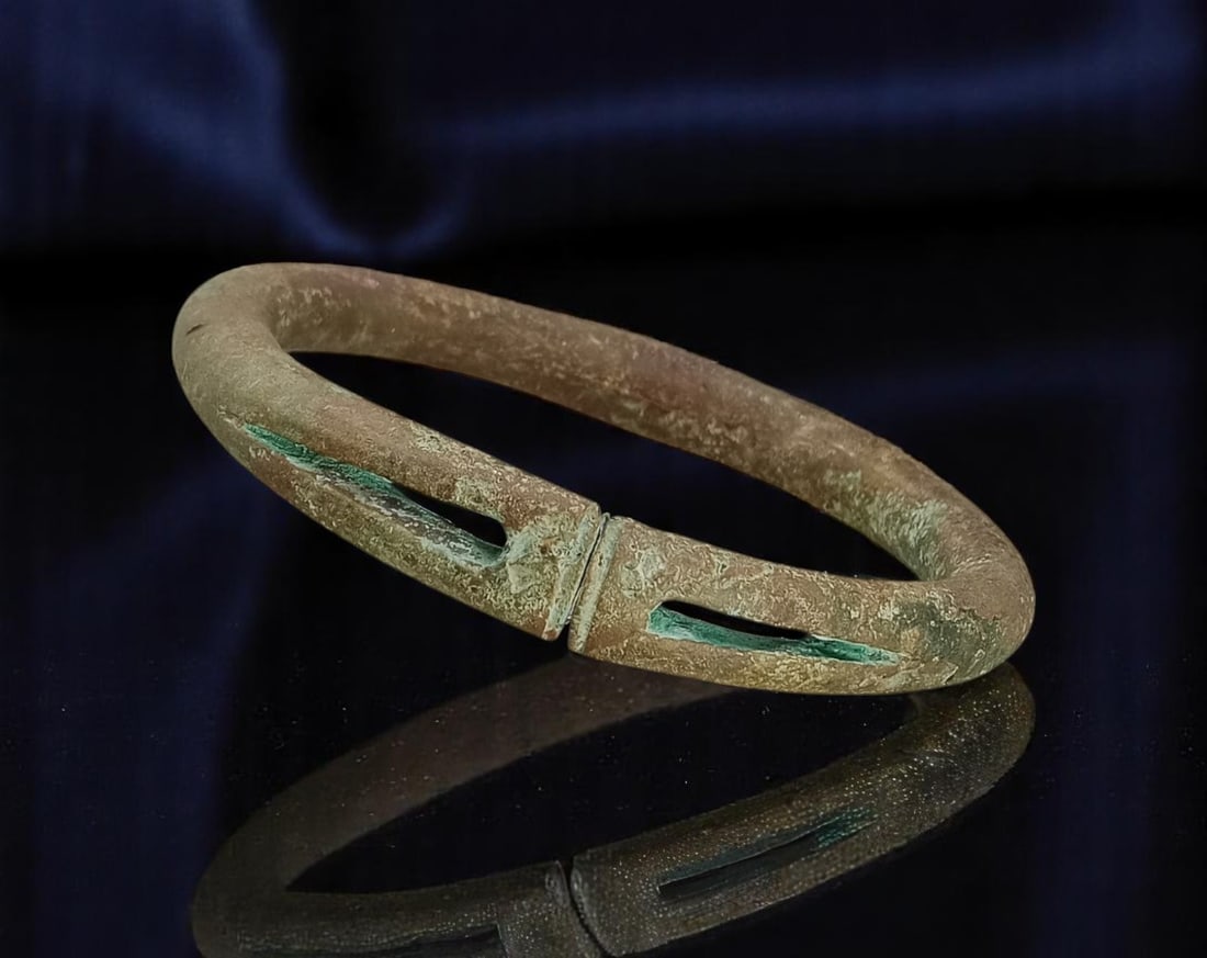 ANTIQUE: Ancient Bronze Bangle - Slotted Ritual Form, Deep Patina, 12cm, 349g: This commanding ancient bronze bangle, sourced from estate antiquities, showcases an oval form with incised slotted cutouts flanking a central banded ridge. With a substantial weight of 349g and a 12c