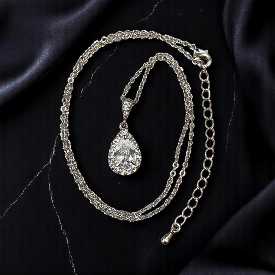 Necklace - Pear-Cut Clear Stone Pendant with Halo Accents, Silvertone Chain, 40cm: A dazzling example of contemporary elegance, this necklace features a brilliant pear-cut clear stone pendant surrounded by a halo of smaller brilliant-cut clear stones, all suspended from a fine silve