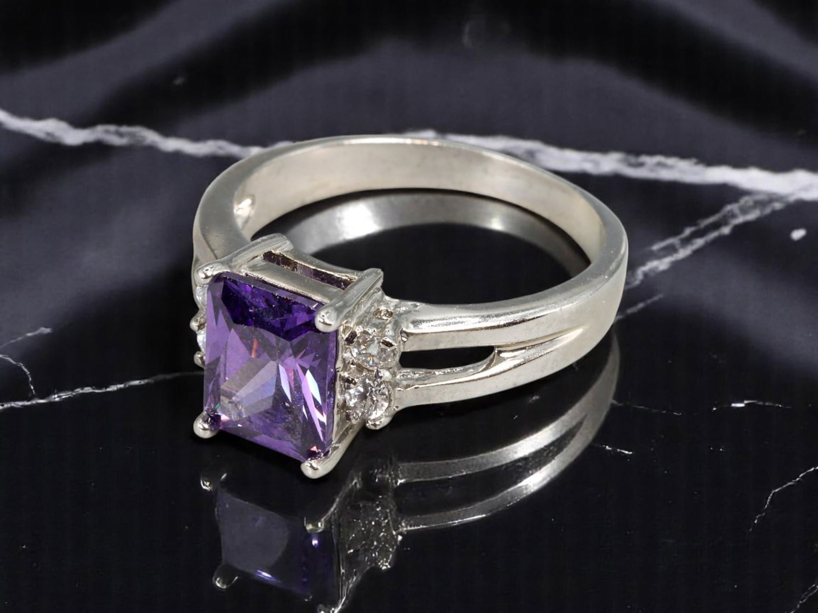 Ring - Emerald-Cut Violet Stone with Cluster Accents, Stamped 10KT, Size 8 US: An elegant vintage-modern ring designed with sculptural flair, this piece features a striking emerald-cut violet center stone, prong-set to maximize brilliance and depth. The flanking shoulders are ad