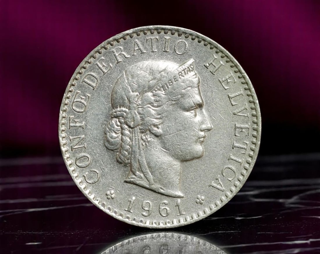 SWITZERLAND: Liberty Ideal - Helvetia 20 Rappen Coin, 1961, 21mm: This 1961 Swiss 20 Rappen coin offers a timeless homage to Helvetia, the allegorical embodiment of the Swiss Confederation. Wearing a laureled crown inscribed ''Libertas,'' she is portrayed in stoic c