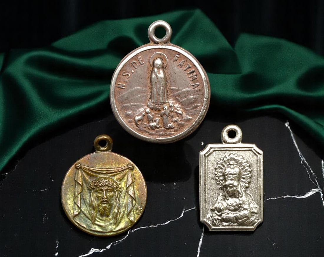 FRANCE/PORTUGAL: Marian Apparition and Passion Symbols Pilgrimage Medallions, 1920-1940, 16-20mm: This diverse trio of mid-20th-century devotional medallions encapsulates key pillars of Catholic pilgrimage culture, blending the mysticism of Fatima, the sorrowful passion of Christ, and regional ven