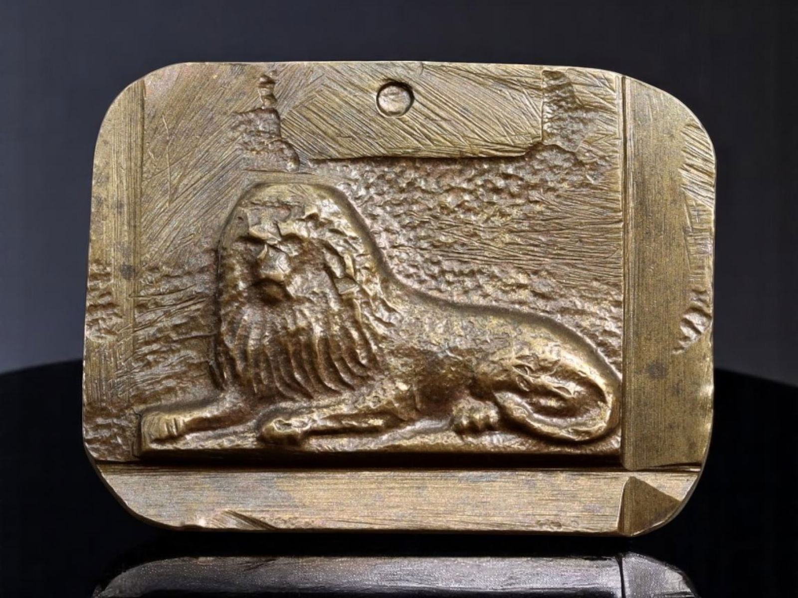 NEOCLASSICAL REVIVAL: Decorative Weight or Medallion - Reclining Lion Relief, Bronze-Tone Cast: A sculptural piece rendered in bronze-tone metal, this compact rectangular form features a deeply cast relief of a reclining lion set against a textured background, framed by angular linear borders. L