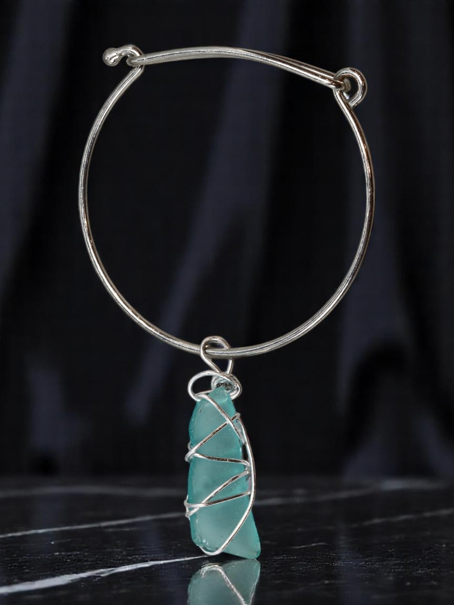 Wire Bangle - Seafoam-Like Wrapped Charm, Silvertone (6.5cm): A minimalist bangle with artisan flair, this silvertone piece features an open wire form with a hand-wrapped charm resembling seafoam-colored glass. The asymmetrical shard is encased in spiraling silv