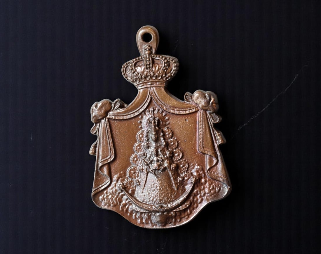 SPAIN: Royal Patronage Virgen del Rocio with Crowned Drapery Frame Devotional Medal, 20th C, 75mm: Rendered in rich bronze tone, this regal devotional piece presents the beloved Virgen del Rocio within an ornate heraldic frame, draped in ceremonial banners and crowned to signify her role as spiritu