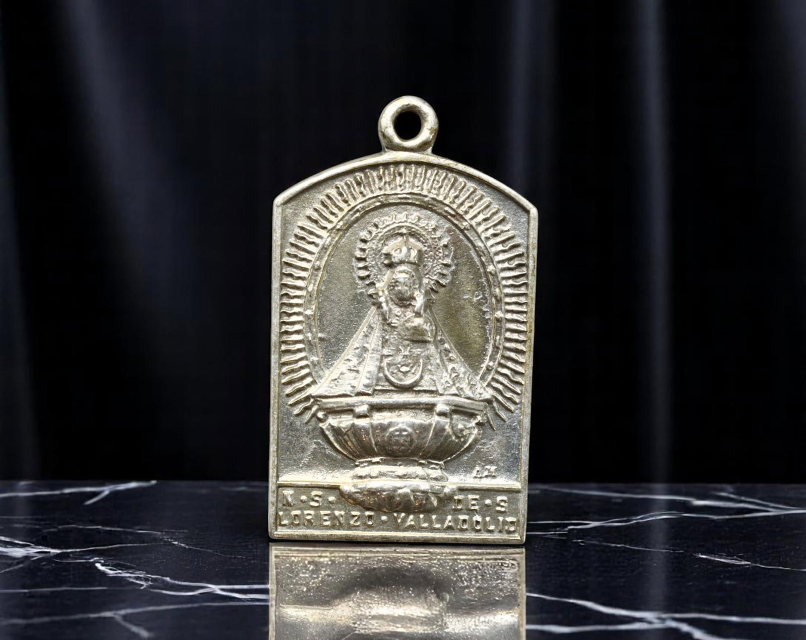 SPAIN: Marian Devotion - Nuestra Senora de San Lorenzo Pilgrimage Medal, Valladolid, 27x15mm: This sharply arched rectangular devotional medal honors Nuestra Senora de San Lorenzo, the revered patroness of Valladolid. Cast in low-relief white metal, the obverse features the crowned Virgin ensh