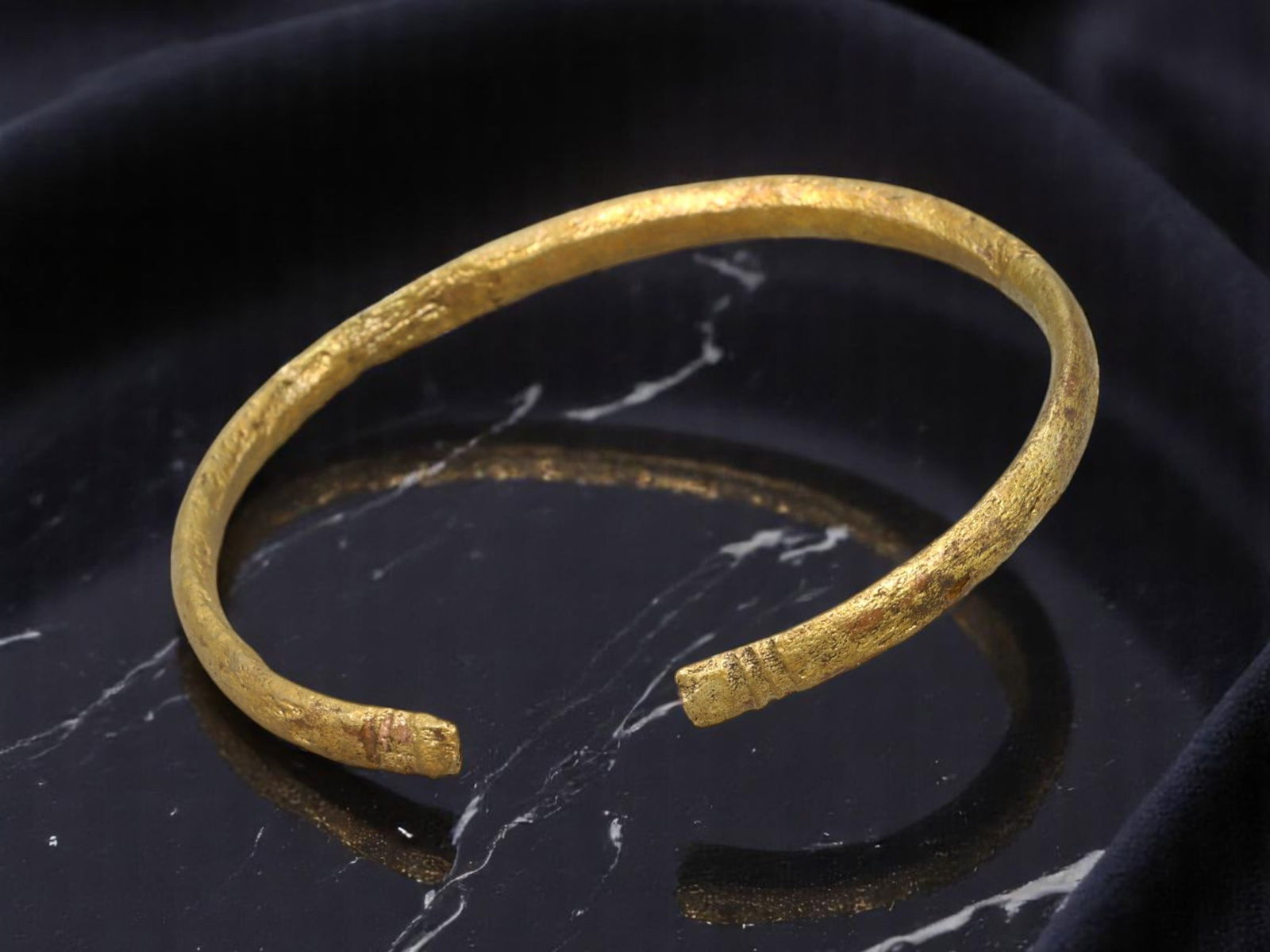 POST-MEDIEVAL Bronze Bangle - Gilt Finish with Incised Banding, Slightly Tapered Terminals, 6.5 cm: A refined yet tactile example of post-medieval bronze jewelry, this open bangle features a subtly tapered silhouette with banded incisions near each terminal. Retaining areas of bright gold-like surfa