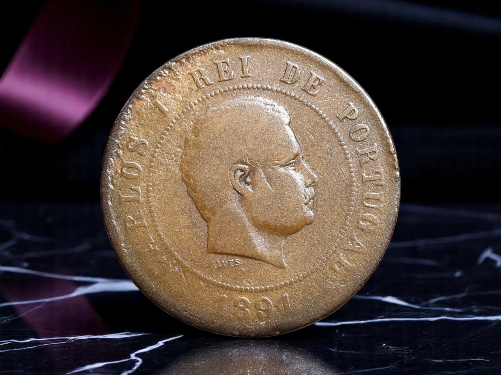 PORTUGAL: Carlos I - Royal Monogram 20 Reis Coin, 1891, 30mm: Struck during the reign of Carlos I, this 1891 20 Reis coin emerges from a Portugal standing at the crossroads of monarchy and modern reform. The obverse displays a composed portrait of the young king