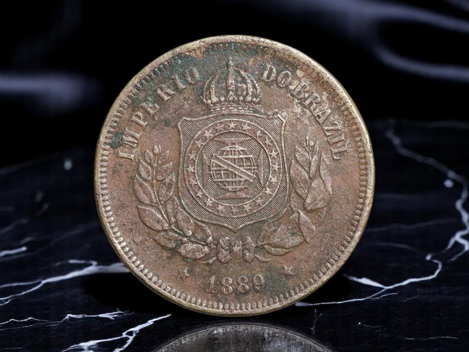 BRAZIL/EMPIRE: Pedro II - Imperial Crest 100 Reis Coin, 1889, 27mm: Minted in the final year of the Brazilian Empire, this 100 Reis coin from 1889 embodies the twilight of monarchic rule under Emperor Pedro II. The crowned national arms dominate the design, flanked by