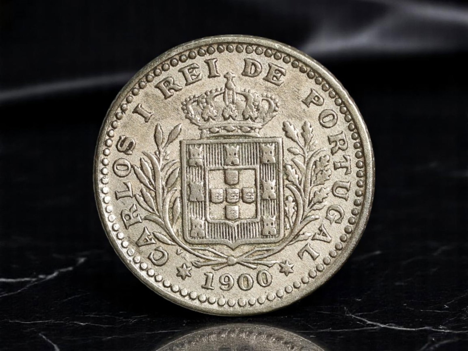 PORTUGAL: Royal Emblem - Carlos I Crowned Arms 50 Reis Coin, 1900, 18mm: Struck at the dawn of the 20th century, this 50 Reis coin from 1900 captures a final moment of Portuguese monarchy in formal elegance. Bearing the crowned arms of Portugal flanked by olive branches, t