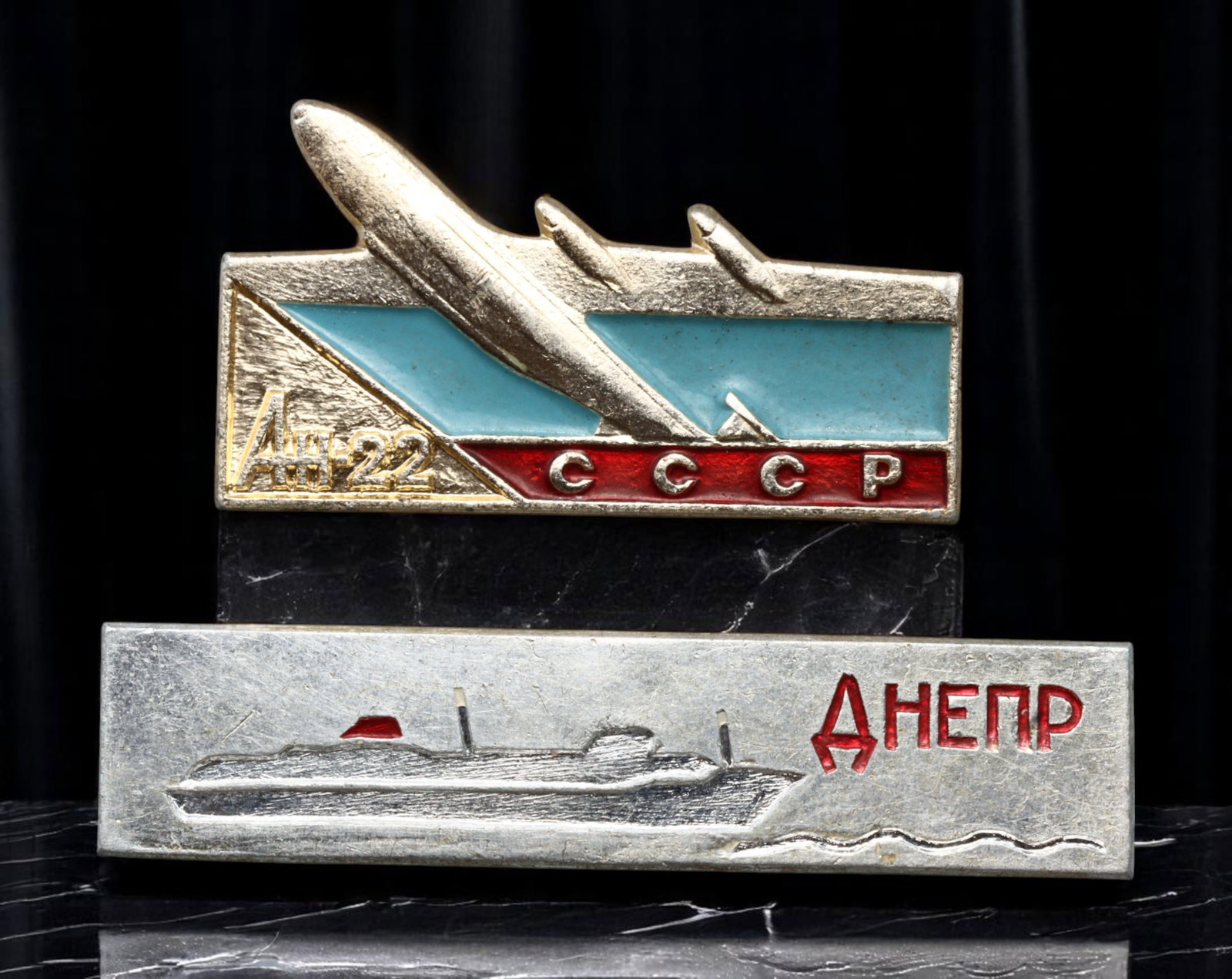 USSR: Aviation and River Fleet Commemorative Badges Pair, 31-43mm: An exceptional duo celebrating Soviet transportation achievements. The first badge depicts the majestic silhouette of the Antonov An-22, the world's largest turboprop aircraft at its debut in 1965, se